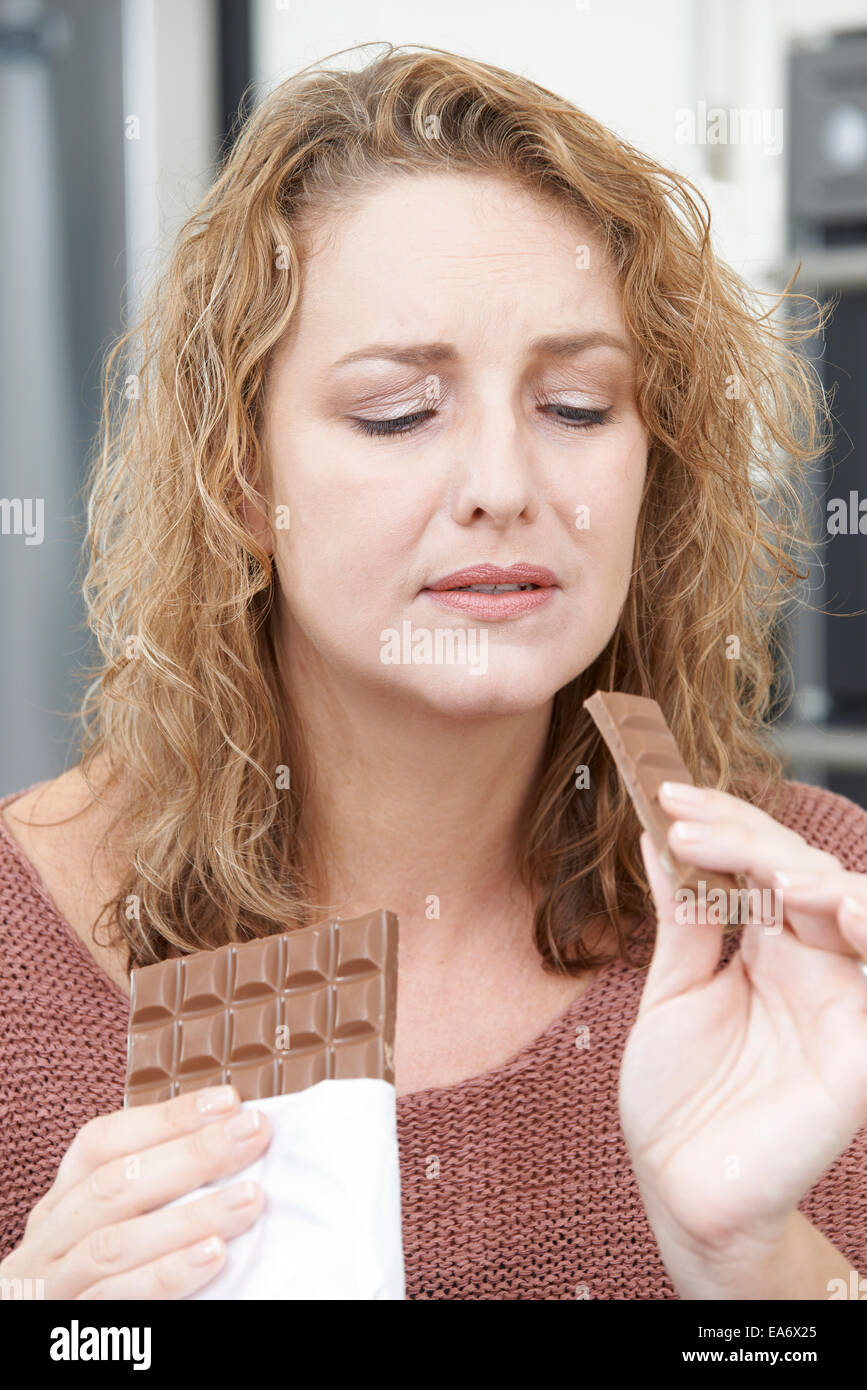 Femme coupable sur le régime alimentaire de manger une barre de chocolat à la maison Banque D'Images