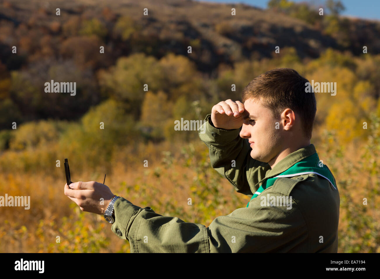 Blindage du scoutisme les yeux contre le soleil avec sa main comme il prend une lecture de son compas magnétique pour trouver son emplacement et th Banque D'Images