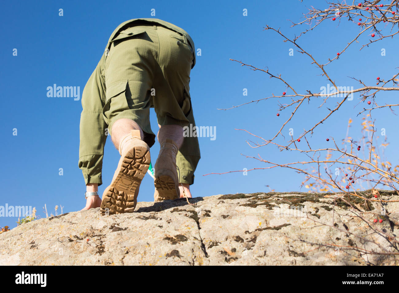 Vue arrière du White boy-scout en uniforme l'ascension d'une grosse pierre sur un climat ensoleillé. Capturé avec fond de ciel bleu clair. Banque D'Images