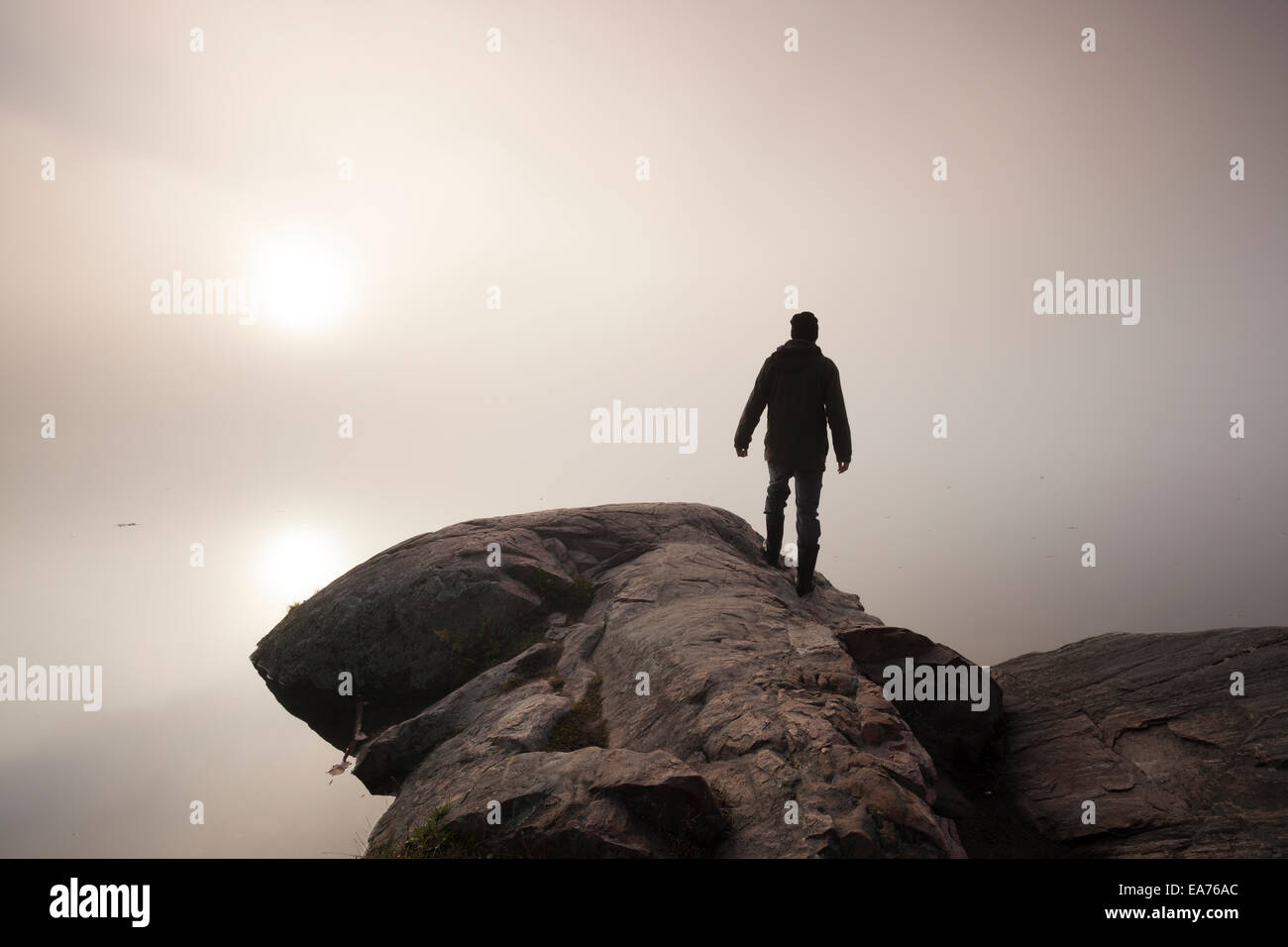 Un homme se tient au bord d'un éperon rocheux à la recherche dans le brouillard que le soleil se lève. Le Parc Provincial Algonquin, en Ontario, Canada. Banque D'Images