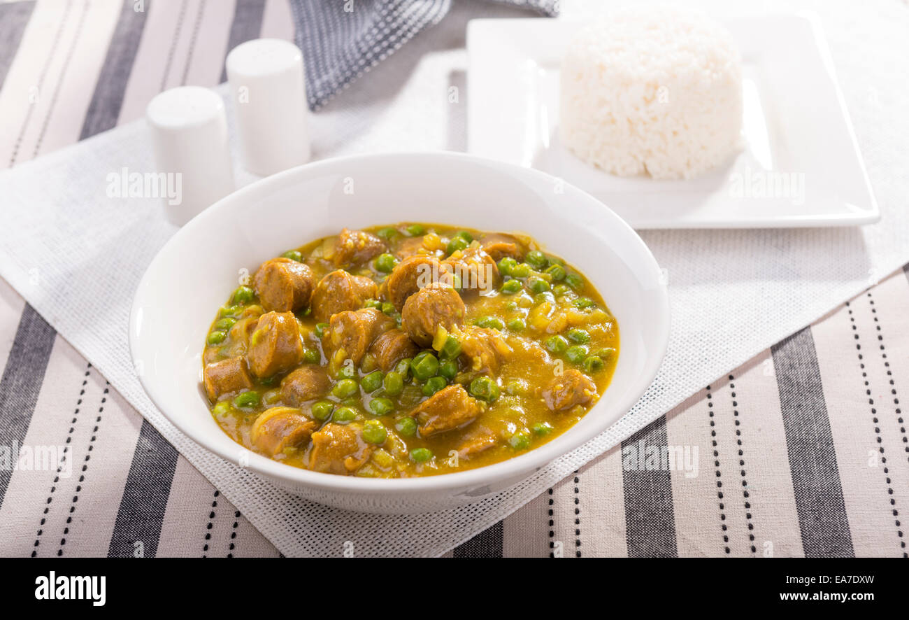 Grand bol de saucisses au curry avec des pois et un côté de riz Banque D'Images