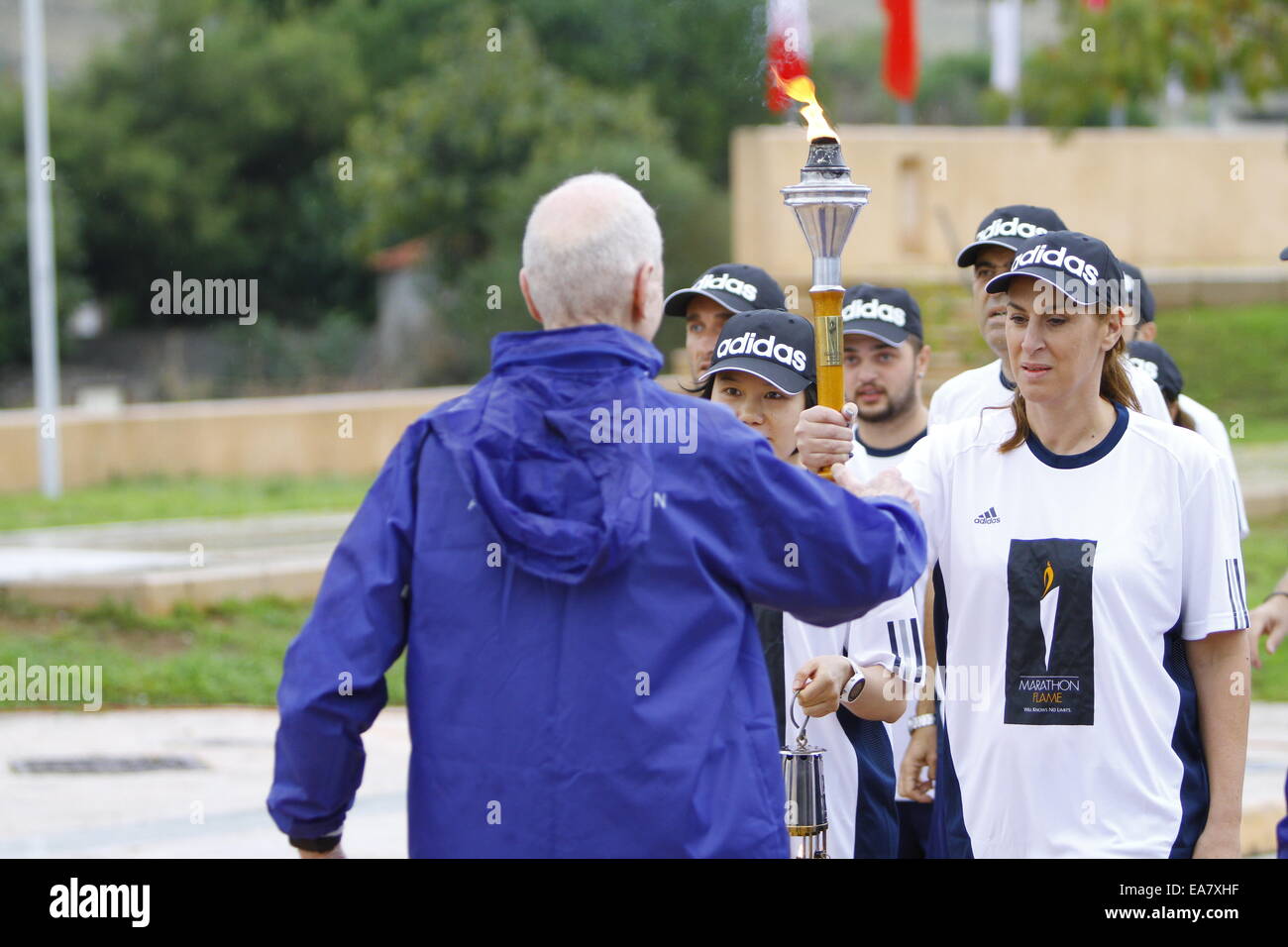 Athènes, Grèce. 8e novembre 2014. Le porteur de flambeau mains sur la torche à flamme Marathon George Hirsch, l'un des fondateurs de la Marathon de New York. La flamme de la 32e Marathon Marathon d'Athènes a été allumé dans le lieu de départ du Marathon à Marathon. La flamme brûlera pour l'ensemble de la week-end marathon. Un nombre record de 13 000 coureurs de marathon est inscrit pour la course de cette année. Crédit : Michael Debets/Alamy Live News Banque D'Images