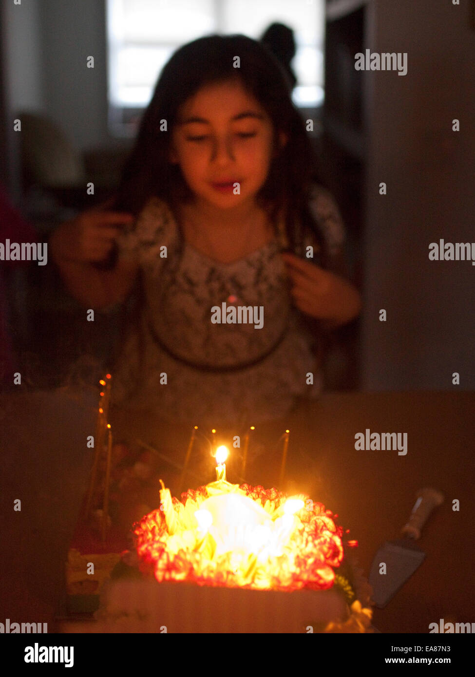 Jeune fille à la maison blowing out candles sur un gâteau d'anniversaire. Banque D'Images