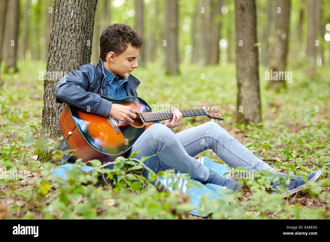 Adolescent qui joue de la guitare dans une forêt en plein air Banque D'Images