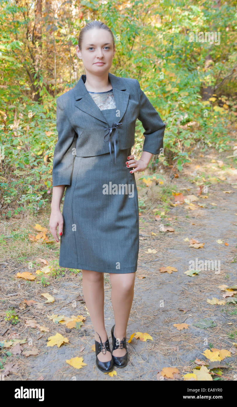 Jolie jeune femme dans une tenue d'affaires gris debout dans la forêt d'automne avec une main sur la hanche Banque D'Images