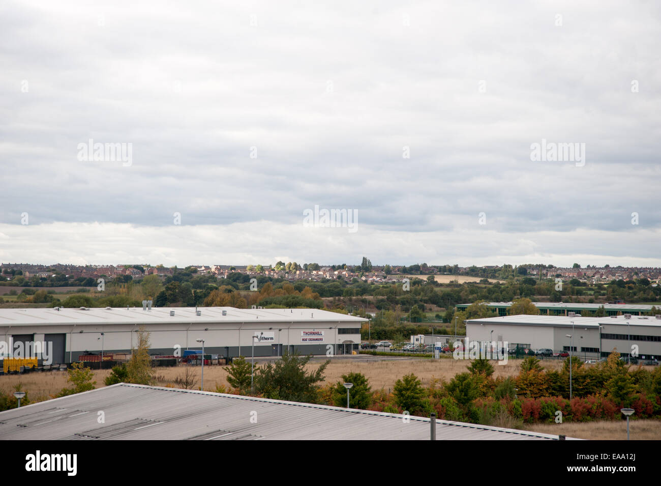 Vue large des entrepôts industriels dans un paysage rural, avec des logements lointains et un ciel nuageux sur une zone à usage mixte. Banque D'Images