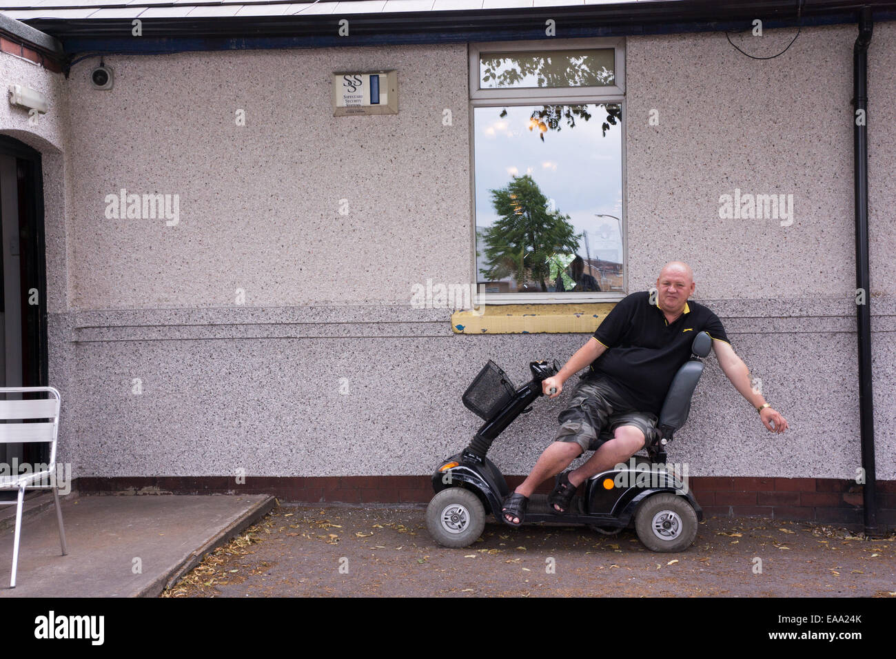 Homme assis sur un scooter de mobilité à l'extérieur d'un bâtiment, se détendre près d'une fenêtre par une journée calme Banque D'Images