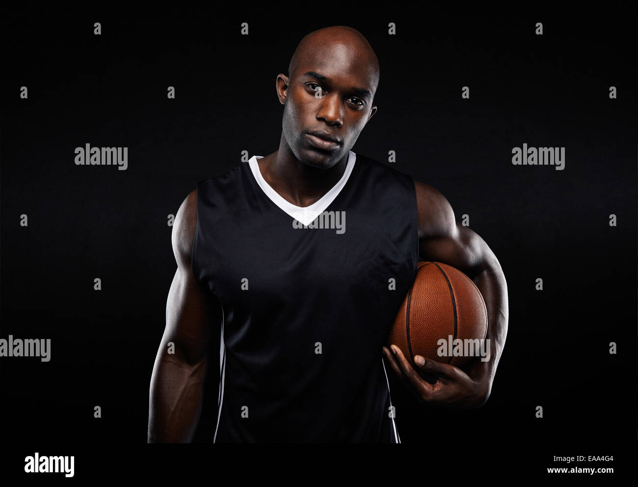 Portrait of young man with strong construire maintenant un terrain de basket sur fond noir. Athlète masculin de l'Afrique. Banque D'Images