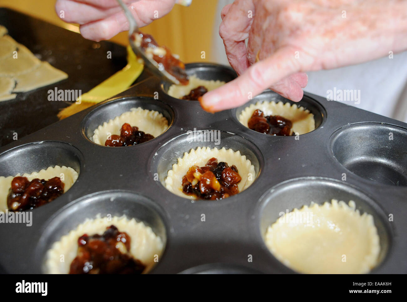 Femme âgée mince pies de cuisson pensionné à la maison dans sa cuisine pour Noël . Mettre la viande hachée dans les coquilles de pâtisserie Banque D'Images