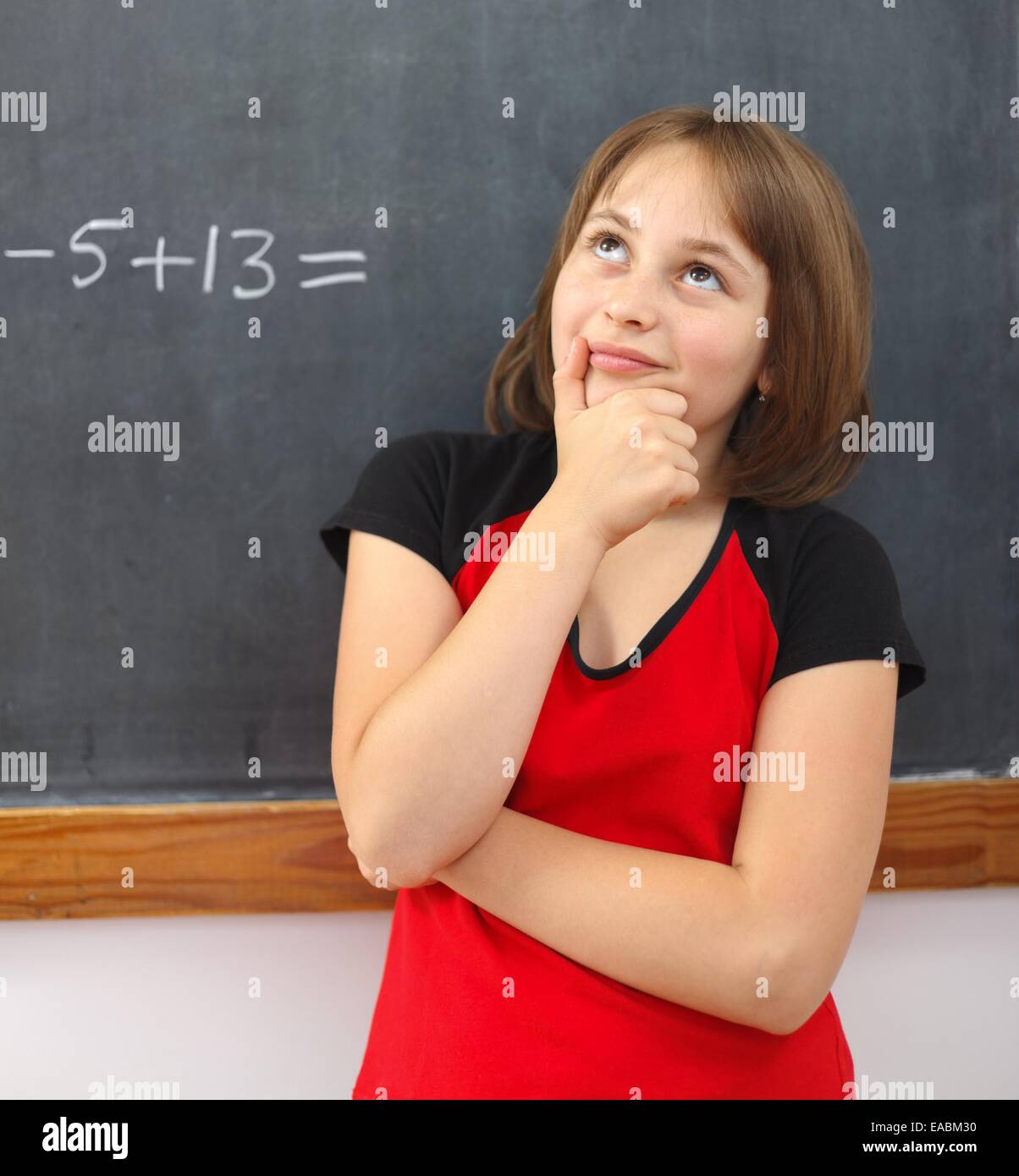 Fille de l'école élémentaire au tableau, réflexion sur la solution de l'équation mathématique derrière elle Banque D'Images