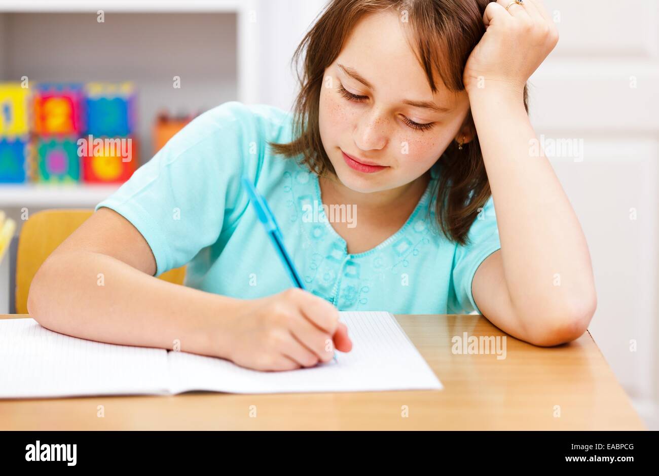 Lycéenne prop sa tête à la main et de l'écriture des devoirs ennuyeux Banque D'Images