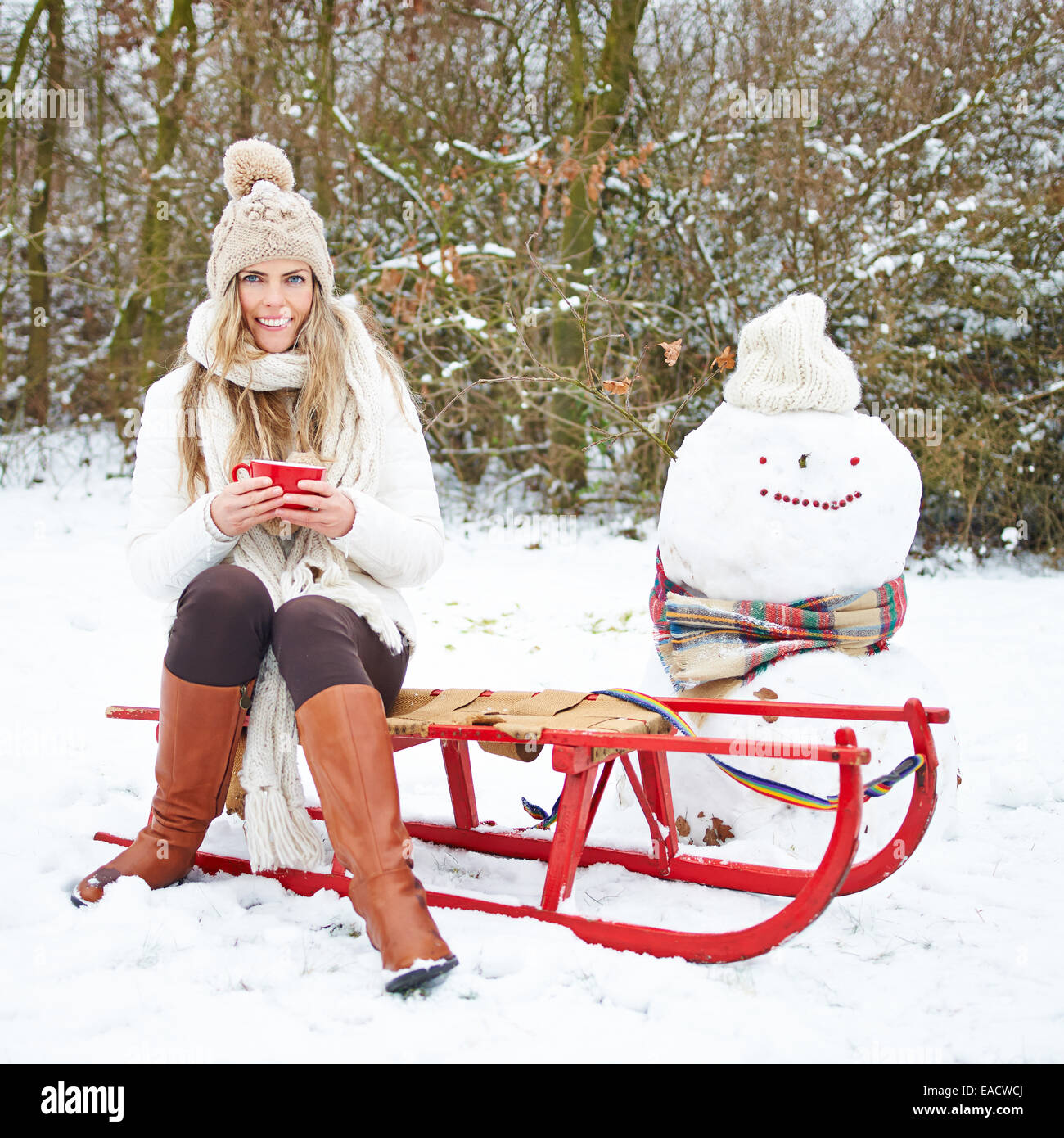 Smiling woman sitting avec plateau en hiver sur un traîneau à côté d'un bonhomme Banque D'Images