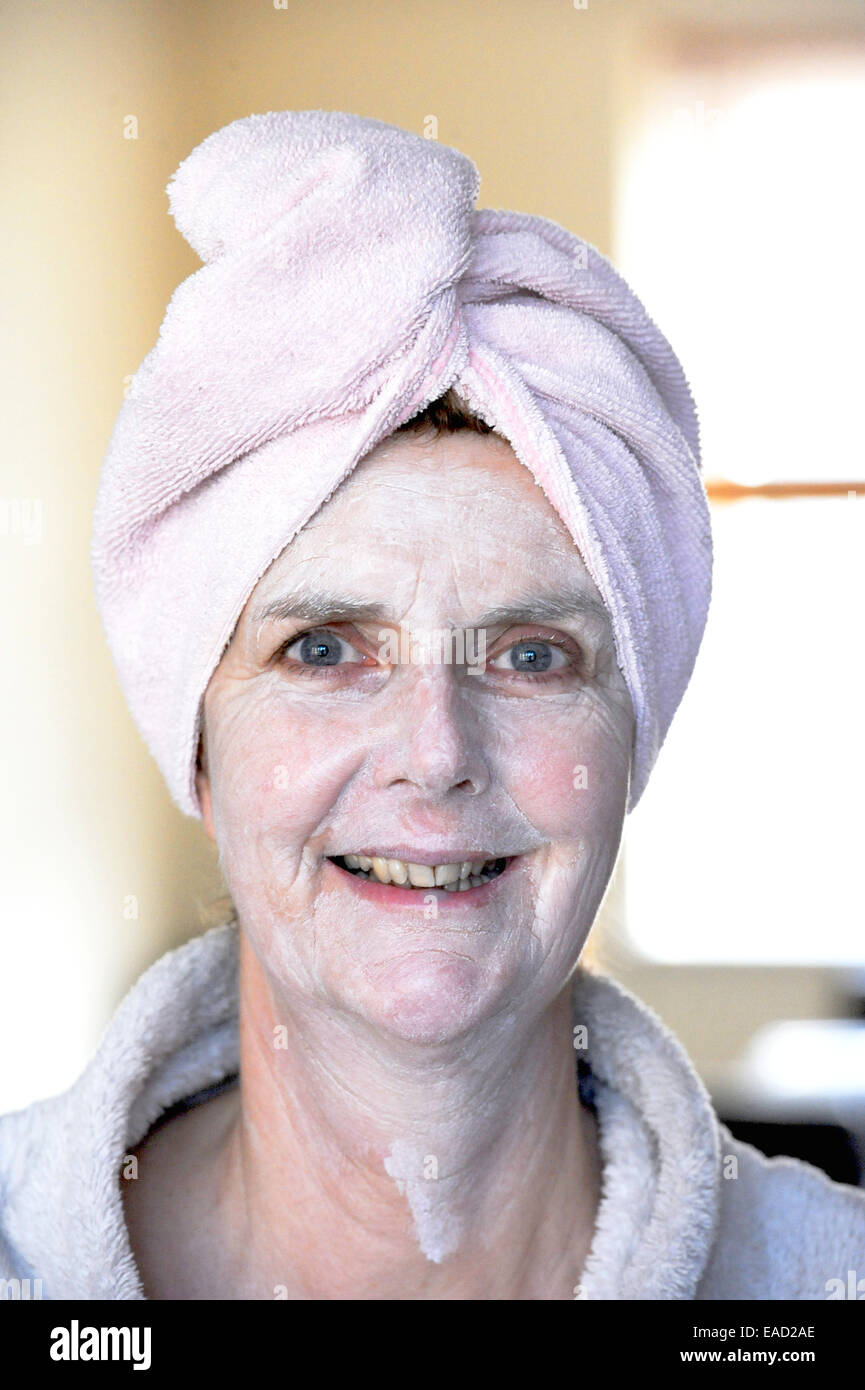 Femme d'âge moyen femme portant un turban sur les cheveux mouillés et à l'aide d'un la santé et beauté visage pack pour la peau Banque D'Images