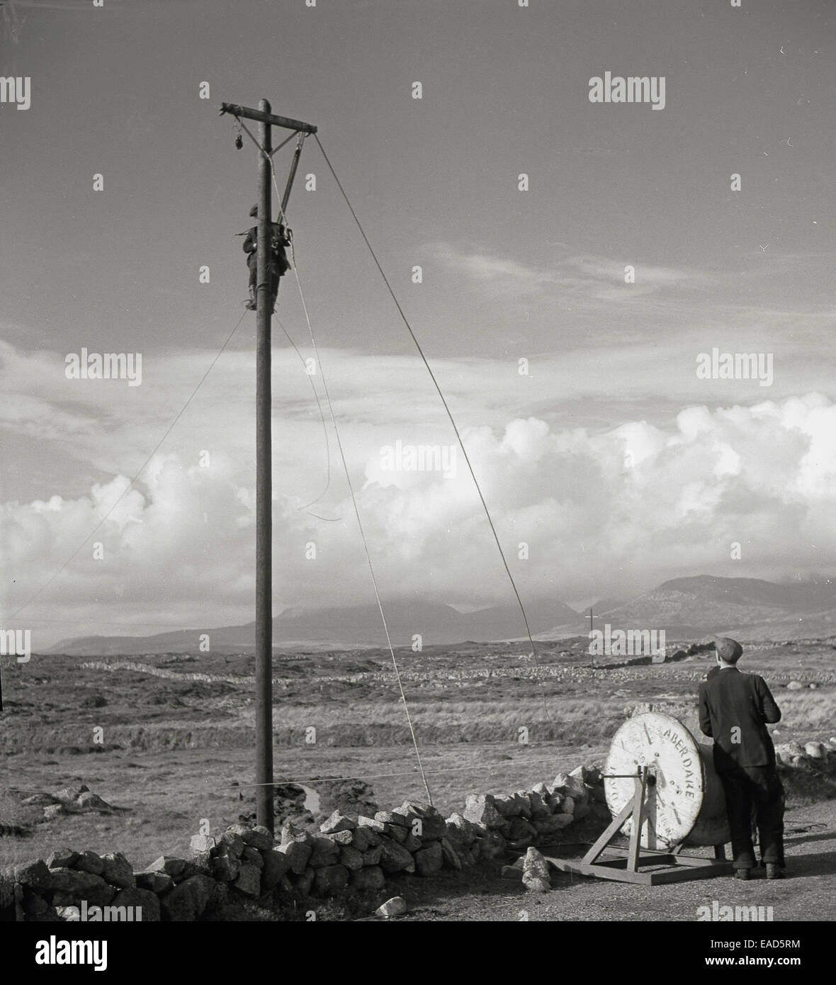 Historique Années 1950 Photo de deux hommes fixant les câbles téléphoniques, un poteau en bois, sur l'un chemin de campagne dans l'Irlande rurale. Banque D'Images