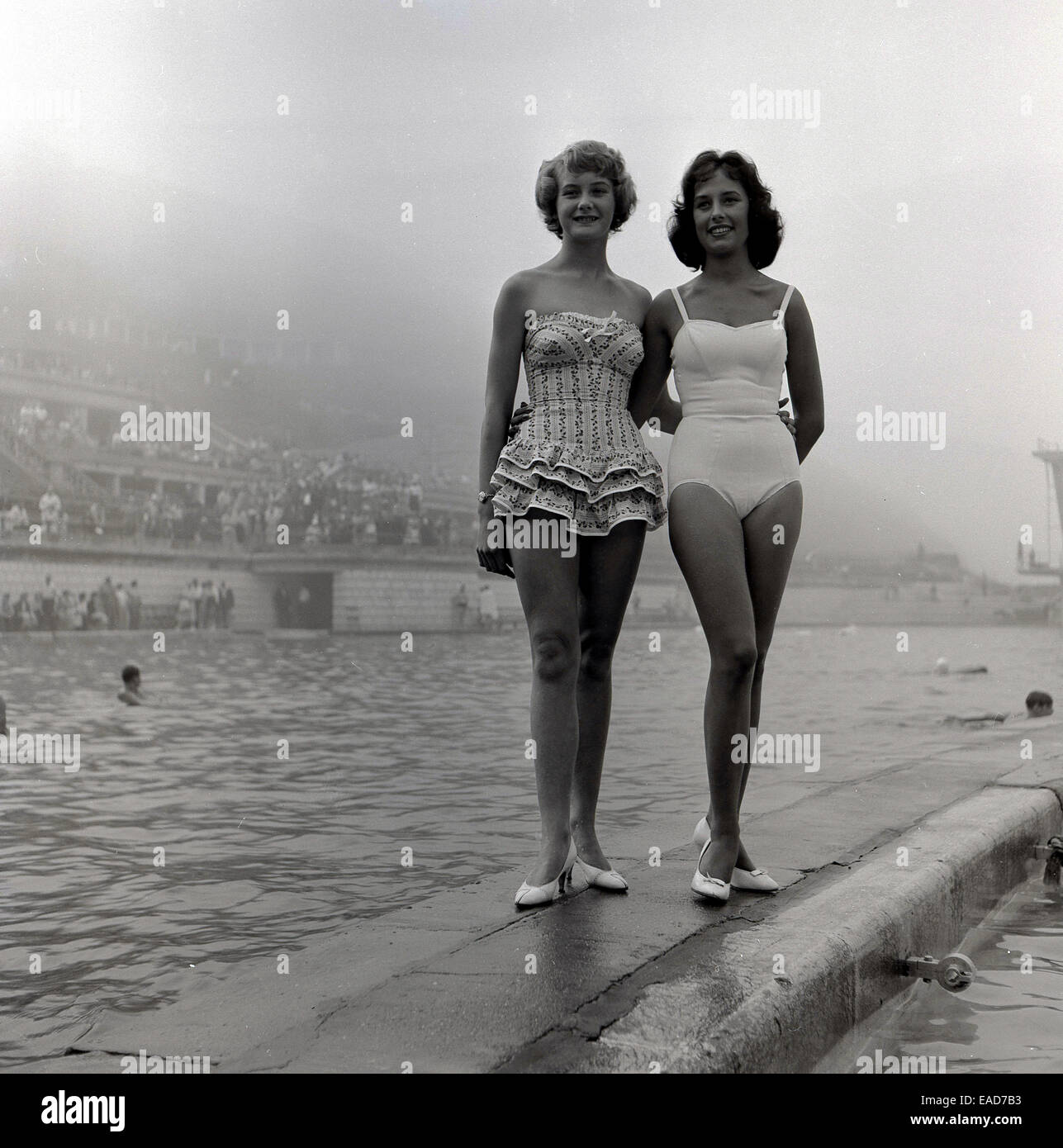 Historique, années 50, deux femmes dans un maillot du concurrent ou de concours de beauté, se tenir ensemble à côté d'une piscine de plein air. Banque D'Images