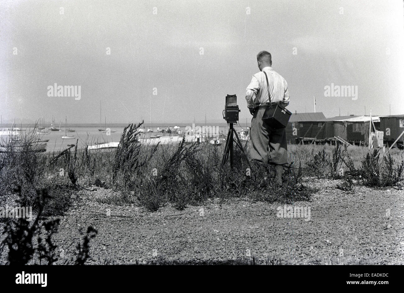 Années 1930, tableau historique d'un photographe masculin à l'aide d'un grand film box de l'époque de l'appareil photo sur un trépied en bois pour prendre une photo de la côte de Norfolk. Banque D'Images