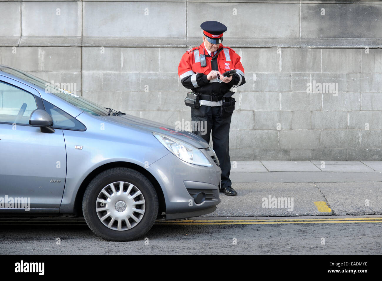 Un gardien de la circulation émet un ticket de parking pour une voiture en stationnement illégal. Banque D'Images