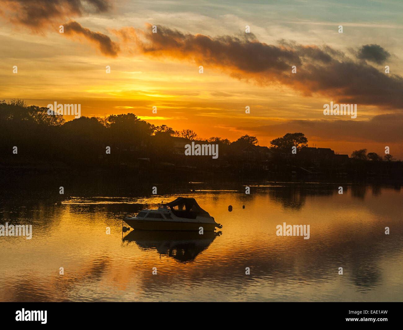 Coucher de soleil sur l'estuaire de Crouch représentant une ligne d'arbres le long de la banque de réfléchir sur une rivière calme avec un petit bateau visible Banque D'Images