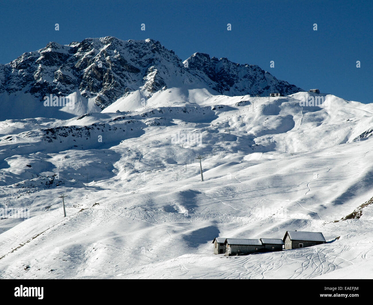Hiver neige scène représentant des bâtiments couverts de neige en premier plan, des sentiers de ski et les montagnes en arrière-plan. Banque D'Images