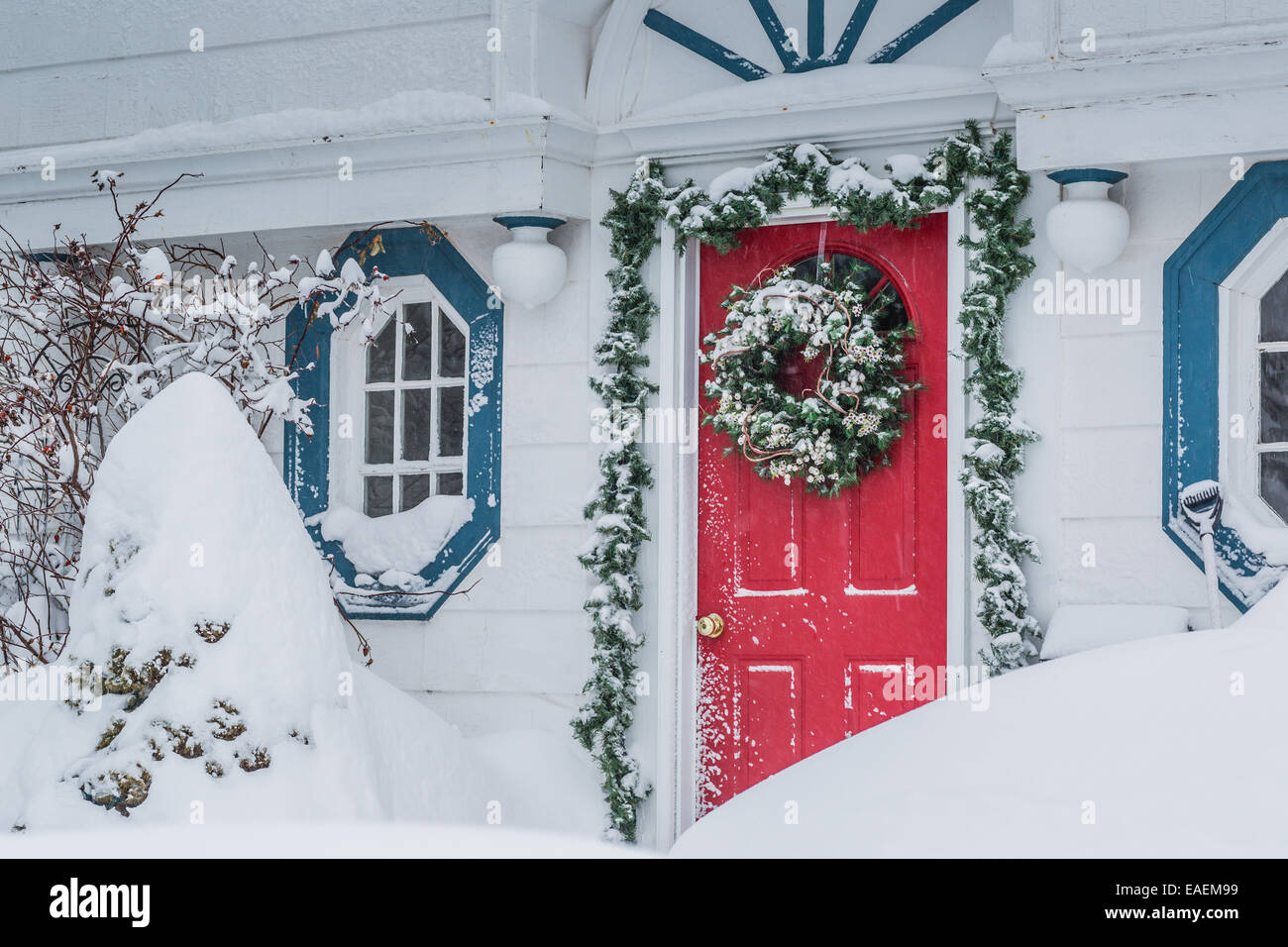 Une porte rouge décoré pour Noël dans une tempête de neige. Banque D'Images