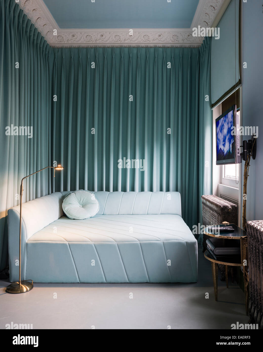 Canapé-lit carré conçu par Moudaber en chambre avec télévision écran plat. Le canapé tissu et rideaux en velours sont de Nya Nordiska Banque D'Images