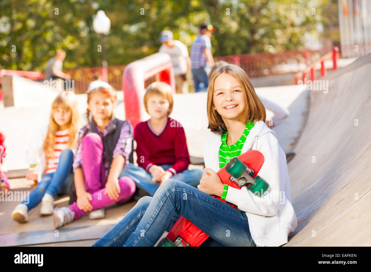 Fille est assise à l'avant avec skateboard et d'autres enfants Banque D'Images