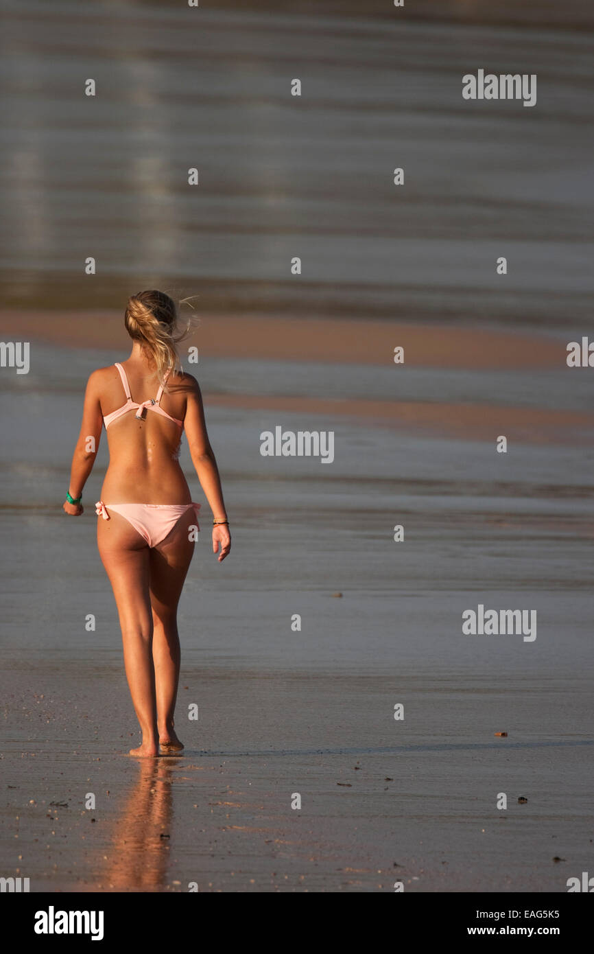 Young blonde woman in bikini marchant le long de la plage Banque D'Images