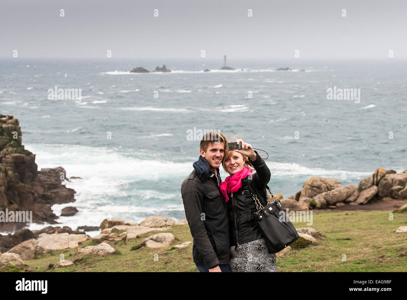 Un couple qui a des terres à selfies fin avec le phare en arrière-plan drakkars à Cornwall. Banque D'Images