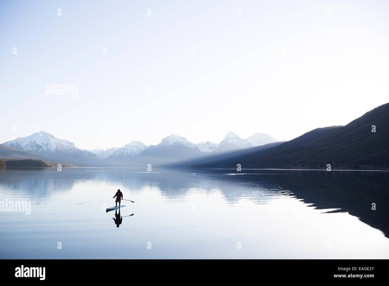 Un homme en stand up paddle (SUP) sur un lac calme McDonald dans le parc national des Glaciers. Banque D'Images