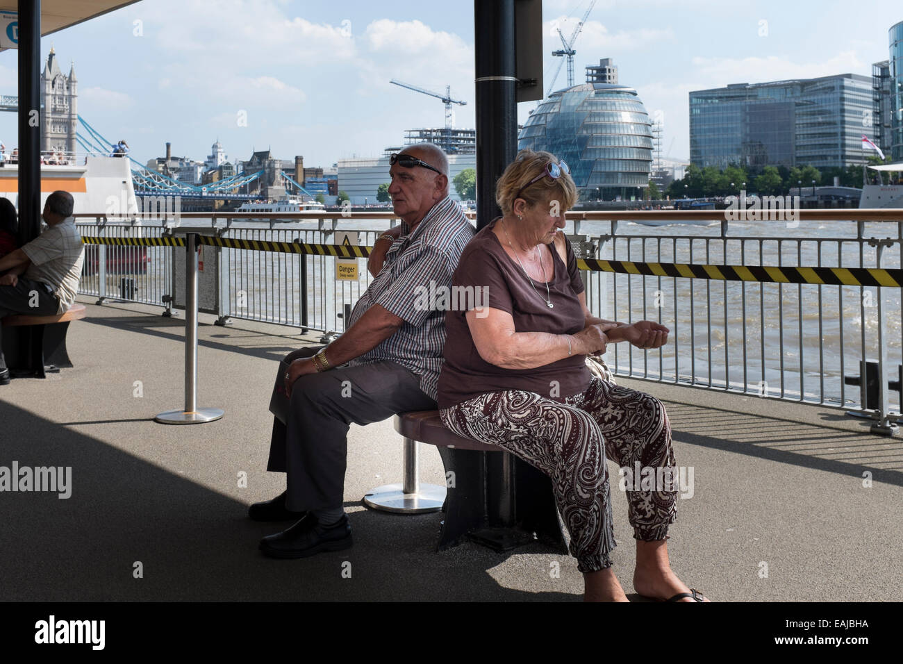 L'homme et la femme assis sur un ponton flottant dans l'attente de l'arrivée d'un bateau touristique sur la Tamise. Banque D'Images