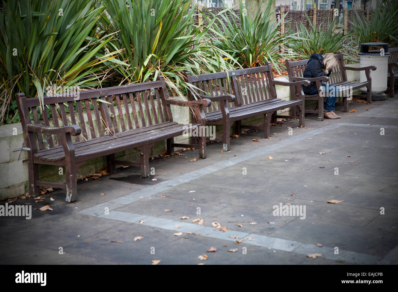 Femme adulte solitaire assis tout seul avec la tête dans les mains assis sur un banc par elle-même, Southport, Merseyside, Royaume-Uni Banque D'Images