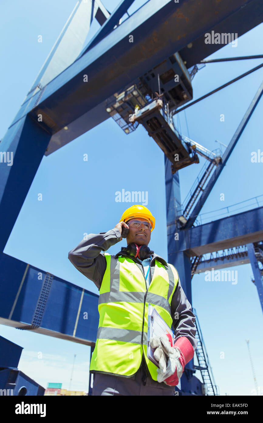 Low angle view of worker talking on talkie-walkie sous grue de chargement Banque D'Images