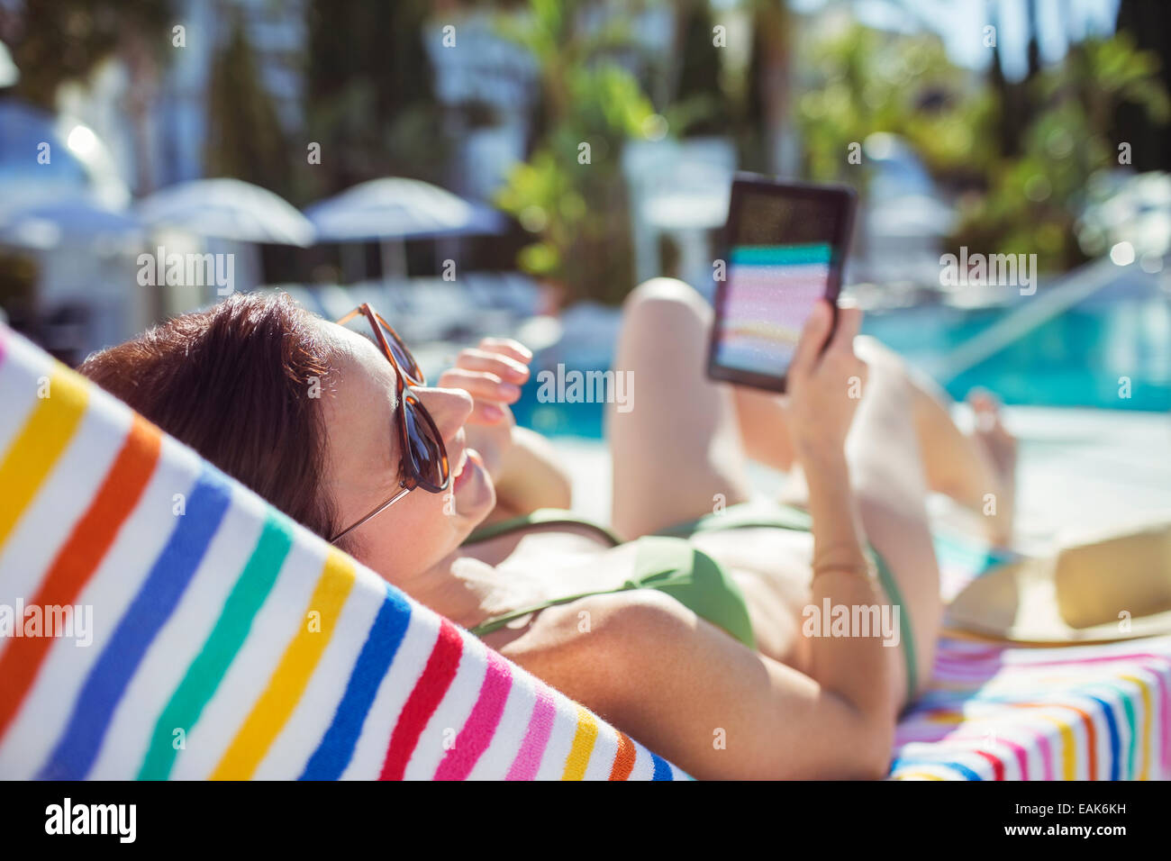 Smiling woman with digital tablet au soleil au bord de piscine Banque D'Images