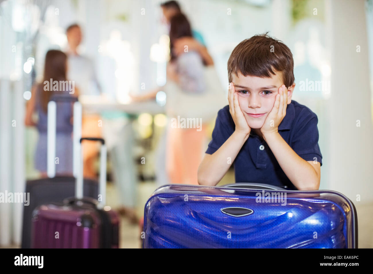Portrait of pensive boy leaning on suitcase in hotel lobby Banque D'Images