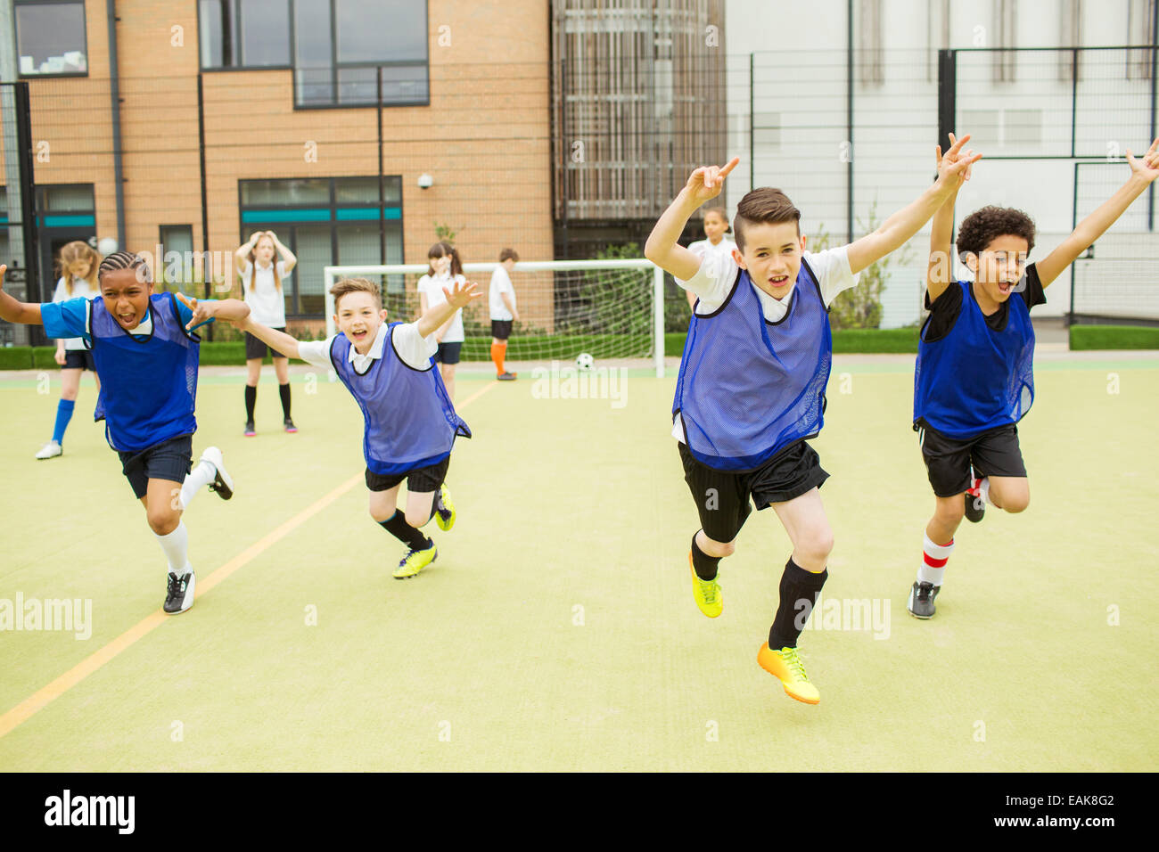 Des écoliers portant des uniformes de sport courir avec les bras levés en terrain de football en face de l'école Banque D'Images