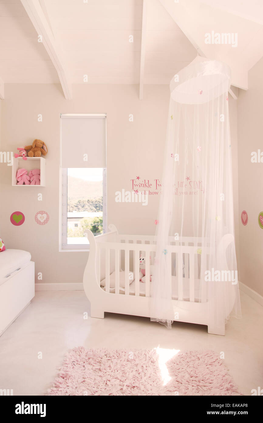 Lit bébé blanc avec tulle auvent dans la chambre de bébé de couleur pastel Banque D'Images