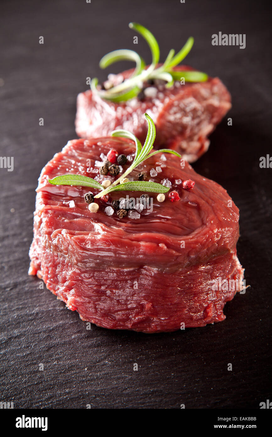 Morceaux de viande rouge steaks avec Rosemary servi sur la surface de la pierre noire. Banque D'Images