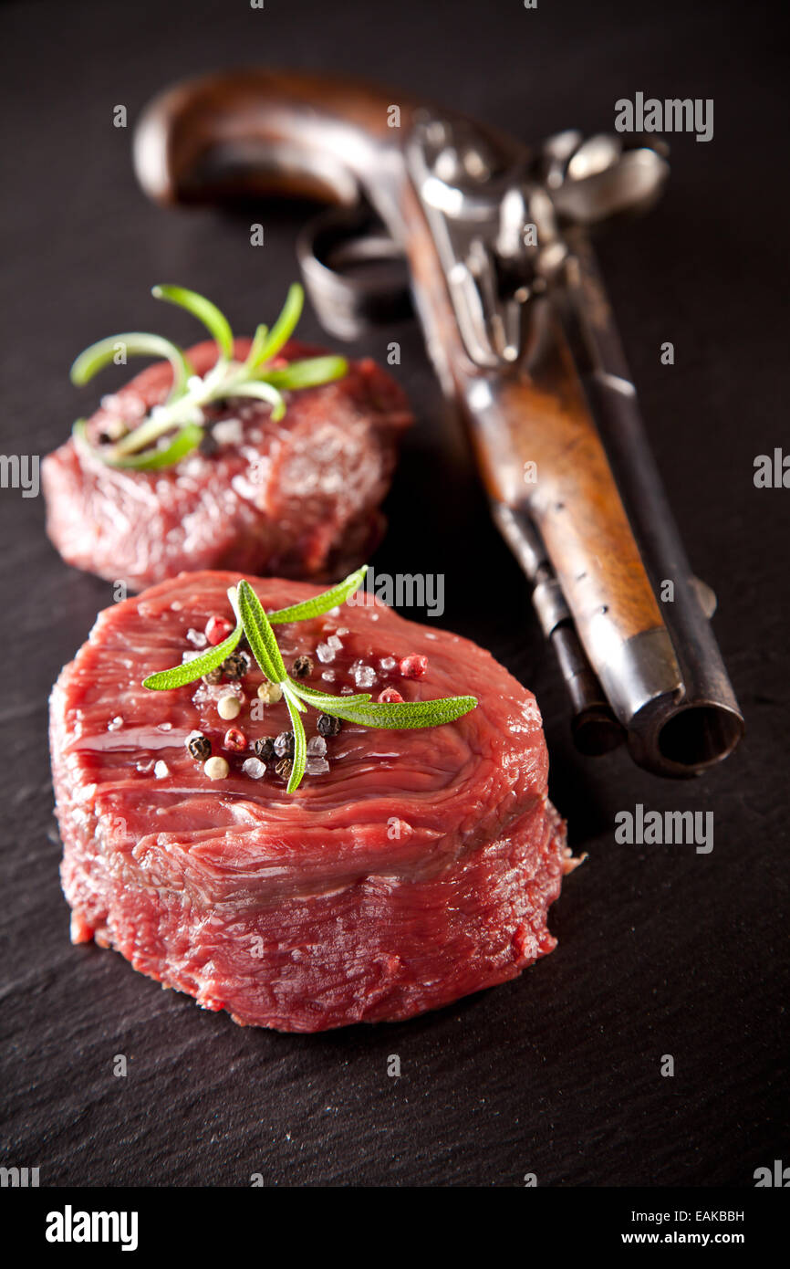 Morceaux de viande rouge des steaks avec de vieux pistolet, servi sur la surface de la pierre noire. Banque D'Images