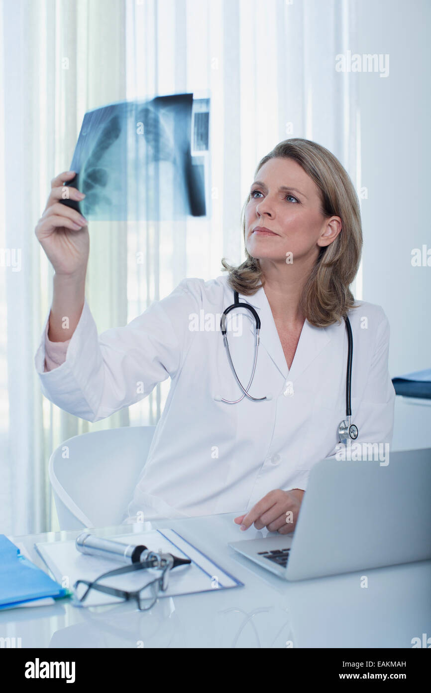 Femme médecin à la recherche de x-ray à 24 avec laptop in office Banque D'Images