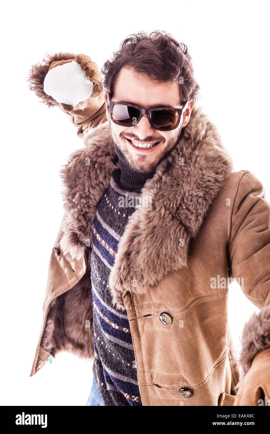 Un jeune homme portant un manteau en peau de mouton isolé sur un fond blanc jouant avec une boule de neige Banque D'Images