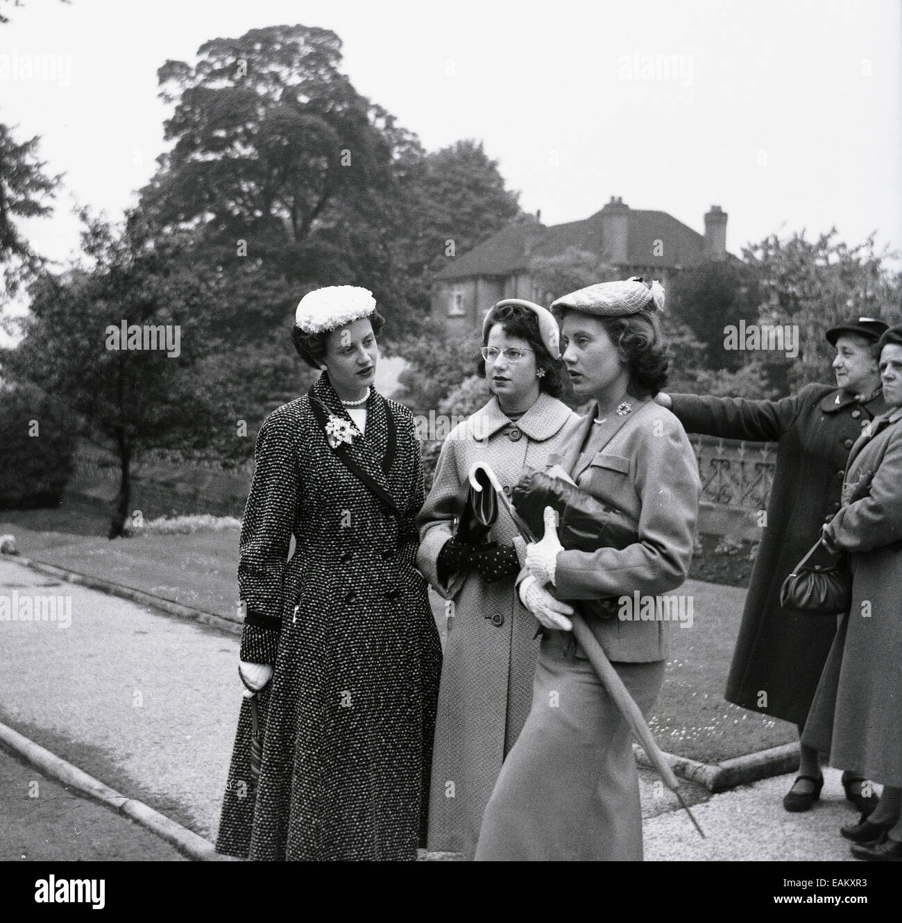 Années 1950, image historique montrant trois jolies jeunes femmes debout ensemble à l'extérieur, élégamment habillées à la mode du jour, avec des chapeaux, manteaux et sacs à main, Angleterre, Royaume-Uni. Banque D'Images