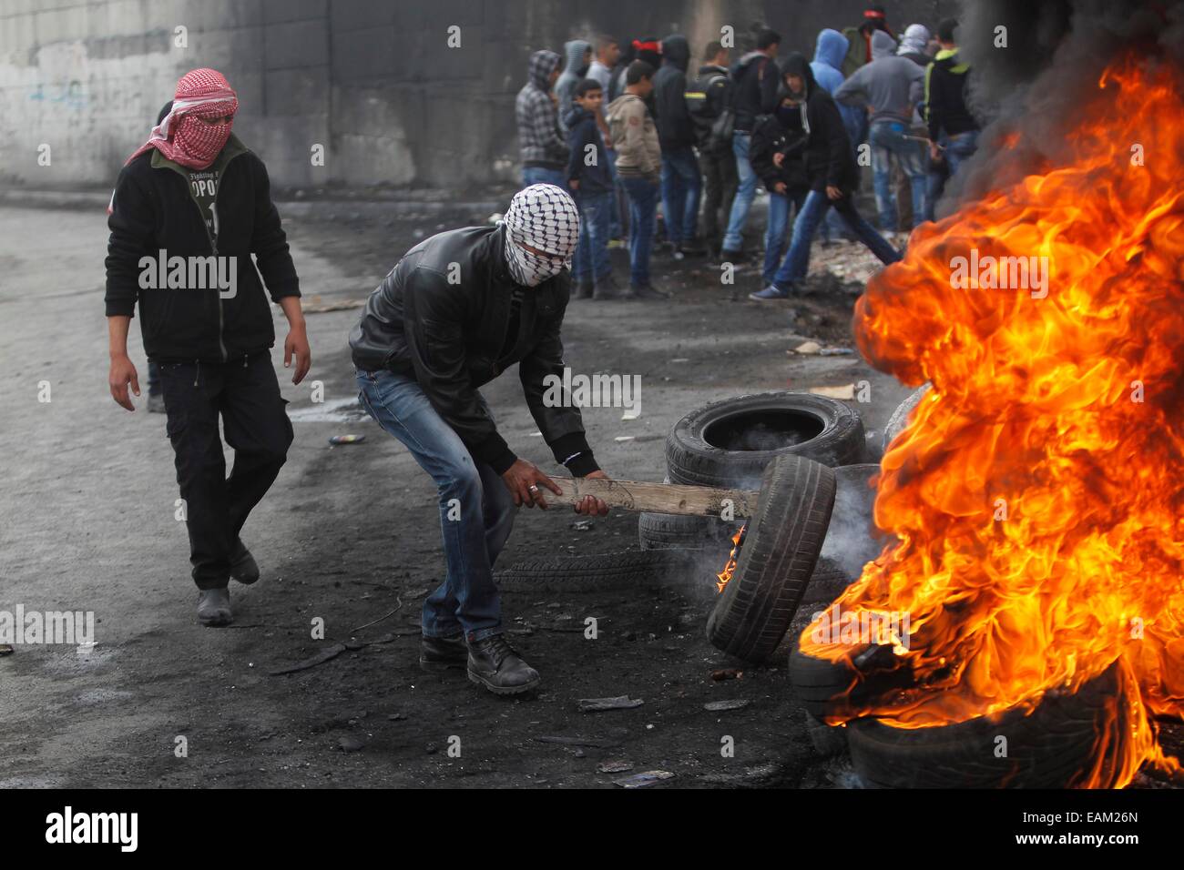 (141117) -- Jérusalem, le 17 novembre 2014 (Xinhua) -- les jeunes Palestiniens masqués brûlent des pneus près de la barrière controversée qui sépare la ville d'Abu Dis, près de Jérusalem, un jour après qu'un chauffeur de bus palestinien, dont la famille vit à Abu Dis, a été trouvé pendu dans son véhicule à Jérusalem, le 17 novembre 2014. Un chauffeur palestinien a été trouvé pendu à l'intérieur de son véhicule à Jérusalem, un incident palestiniens faute sur 'les colons juifs', tandis qu'Israël a dit que c'était un suicide apparent. Tard dimanche soir, le corps de Yusuf Hassan al-Ramouni, 32 ans, a été découvert pendu à l'intérieur d'un bus garé à l'autobus de Jérusalem Banque D'Images