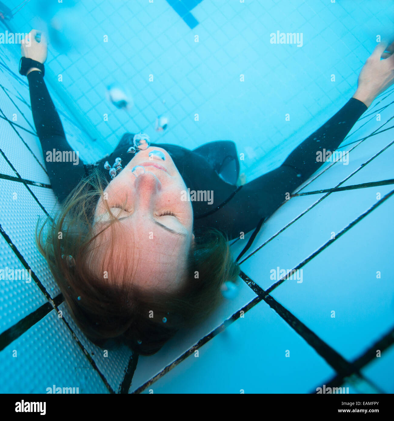 Plongeur sous-marin femelles adultes se concentre avec les yeux fermés en coin de piscine Banque D'Images