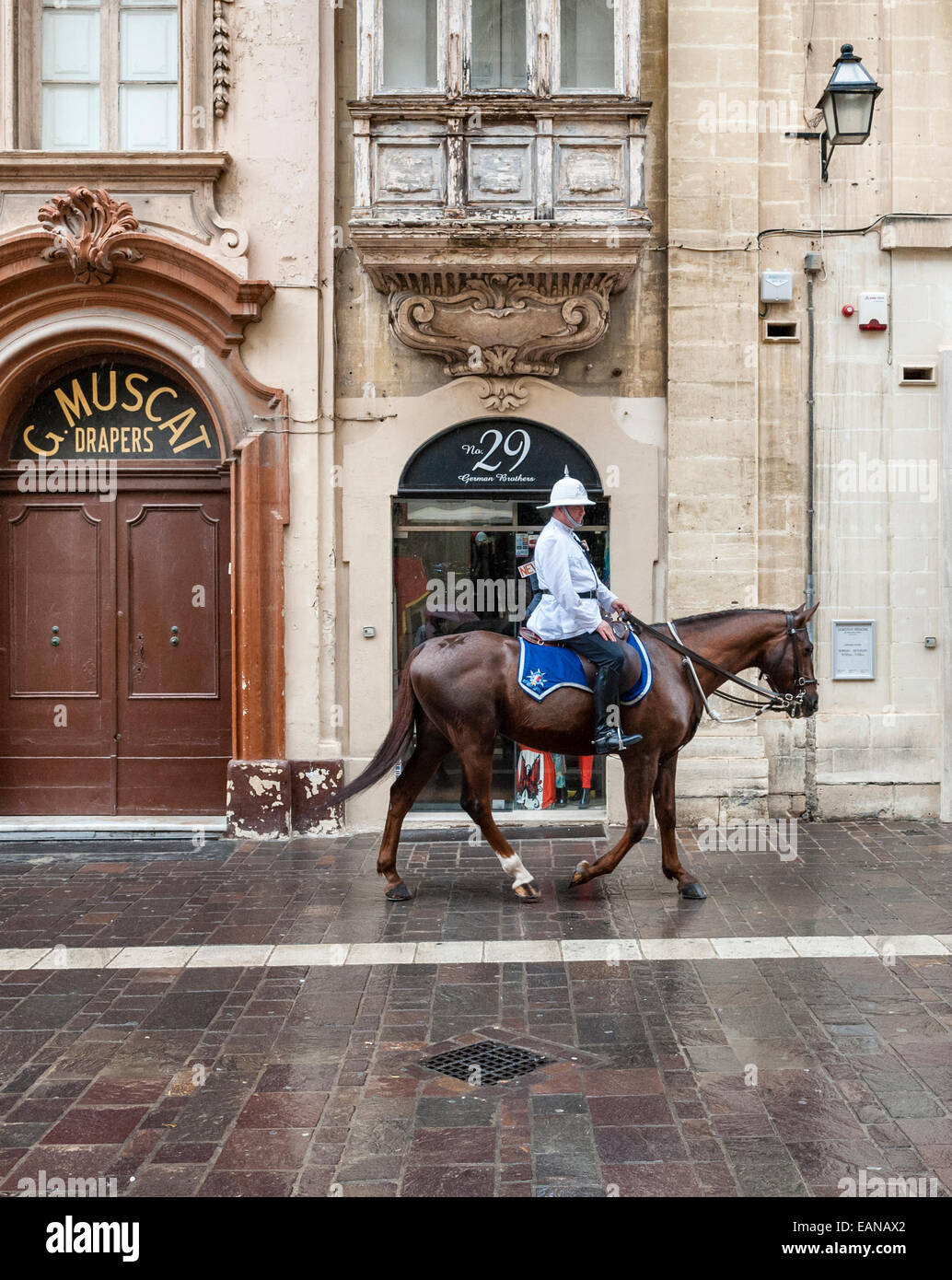 Un policier monté dans son uniforme blanc et son casque de moelle chevauchant dans la rue devant de vieux magasins à la Valette, Malte Banque D'Images