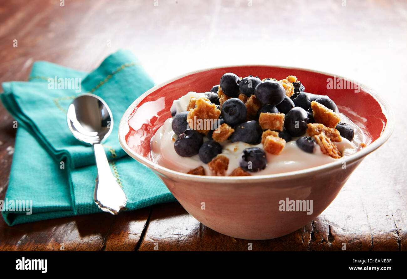 Le yaourt avec les bleuets frais dans un bol avec un petit-déjeuner orange cuillère en argent turquoise sur une serviette sur une table en bois antique Banque D'Images