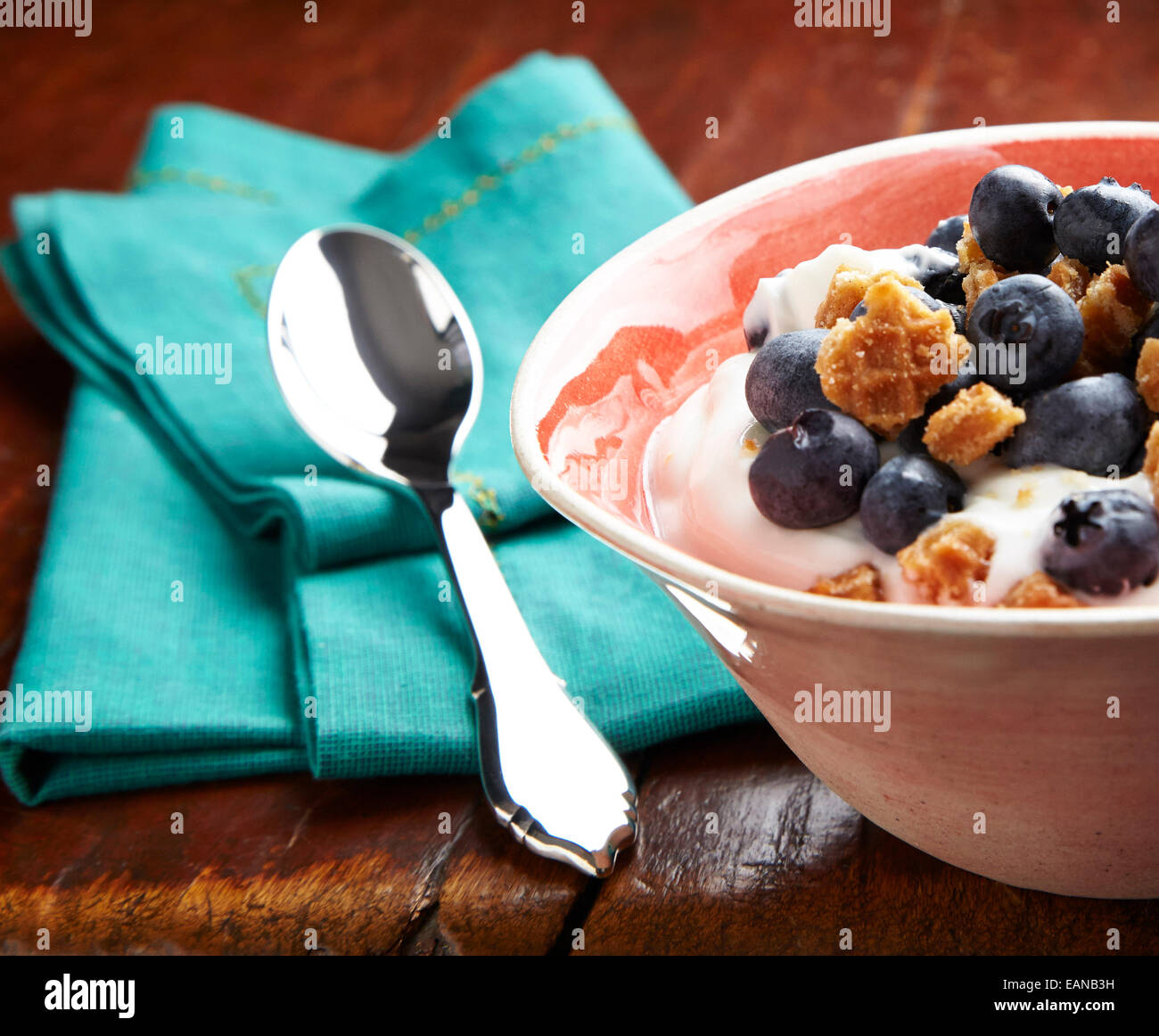 Le yaourt avec les bleuets frais dans un bol avec un petit-déjeuner orange cuillère en argent turquoise sur une serviette sur une table en bois antique Banque D'Images