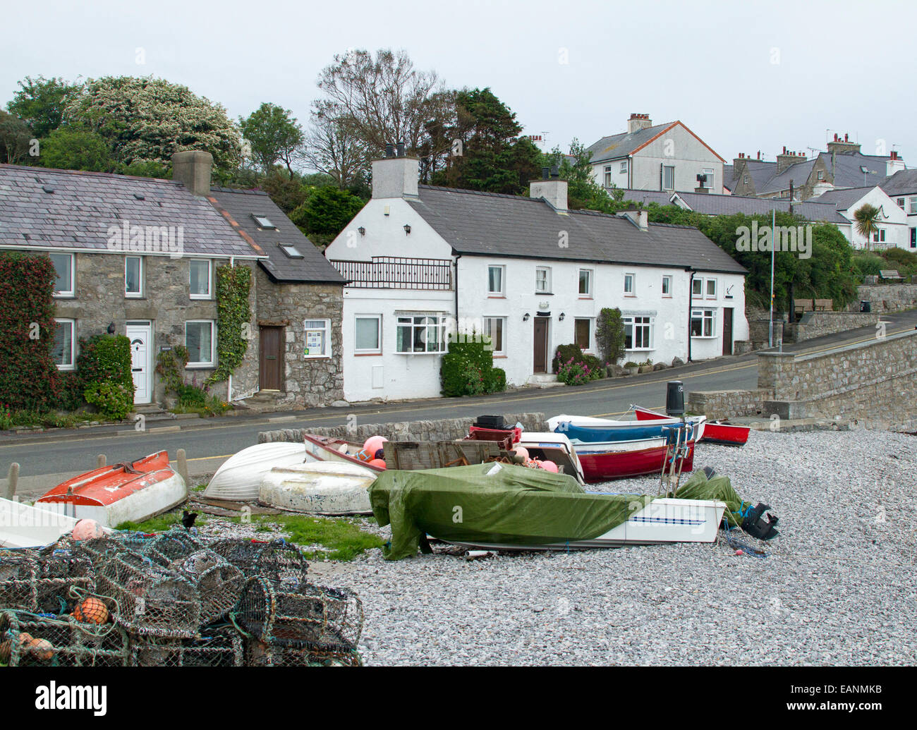 Cottages à côté de route à travers le village gallois de Llangefni avec des bateaux sur la plage de galets voisine Banque D'Images