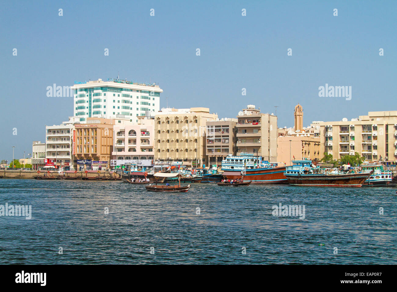 Les boutres traditionnels en bois colorés et en bateau-taxi (ABRA) sur les eaux cristallines de la Crique de Dubaï avec des bâtiments de la ville adjacente de Dubaï s'élevant dans le ciel bleu Banque D'Images