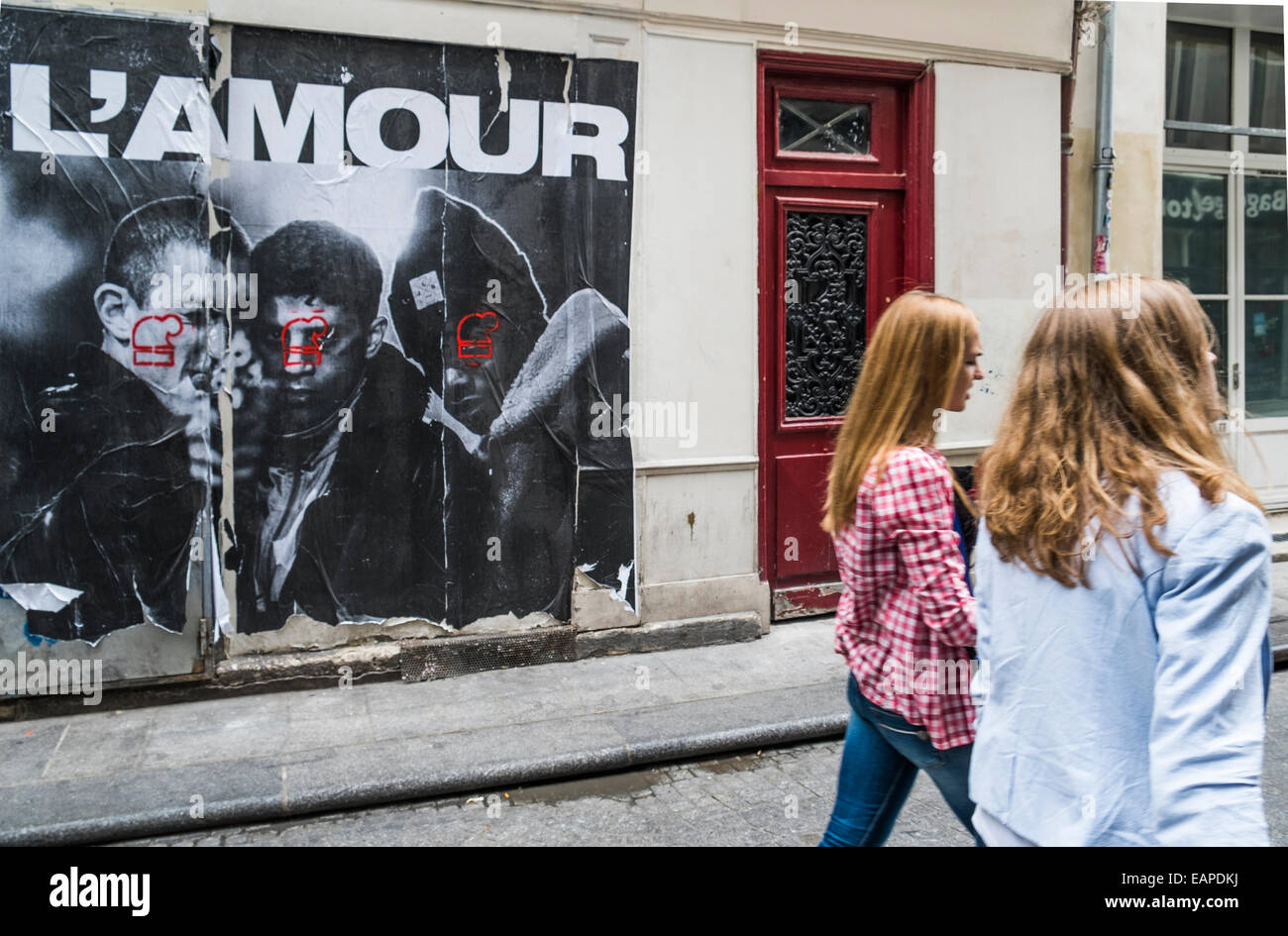 Deux jeunes femmes en passant par une affiche sur un mur montrant trois jeunes l'un d'eux tenant un pistolet, et les caractères en haut de l'affiche Banque D'Images