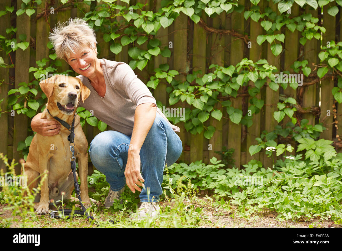 Smiling woman sitting avec un chien dans un jardin en été Banque D'Images